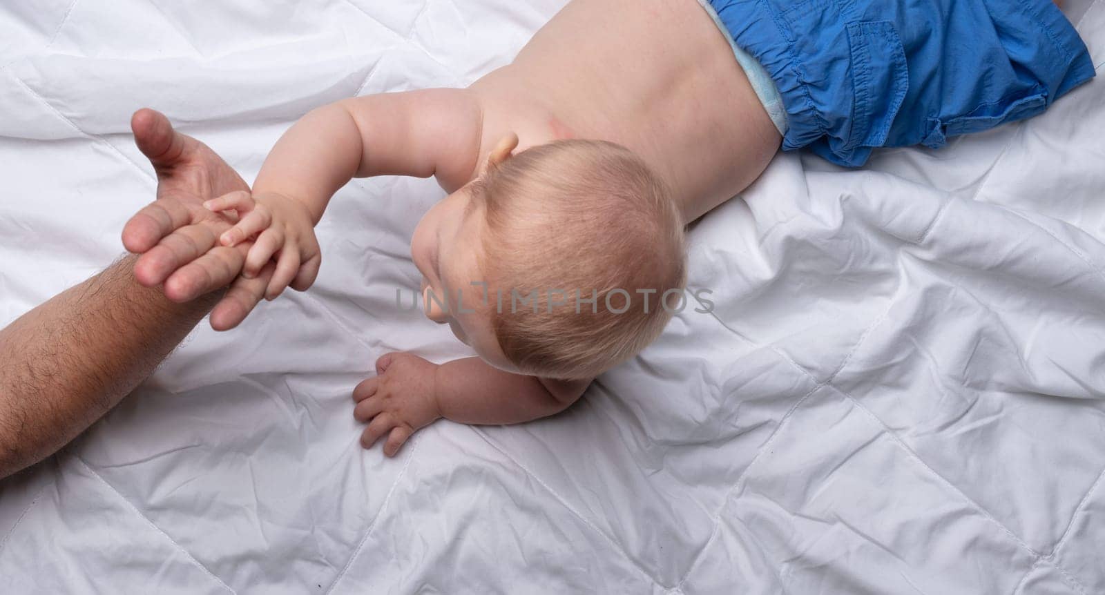 Loving father reaching out to his newborn baby son touching hands as they spend quality time together on a bed