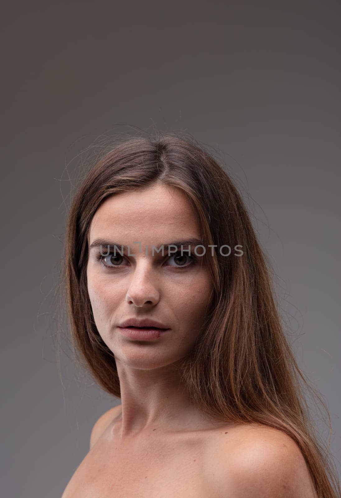 Intense beautiful young woman turning to stare at the camera with large wide open brown eyes and parted lips on a grey studio background