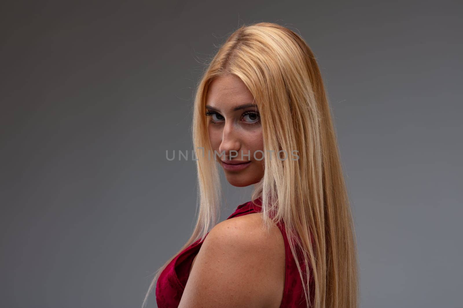 Seductive young woman with a sultry expression turning to look quietly at the camera over her shoulder in a head and shoulders portrait against a grey studio background with copyspace