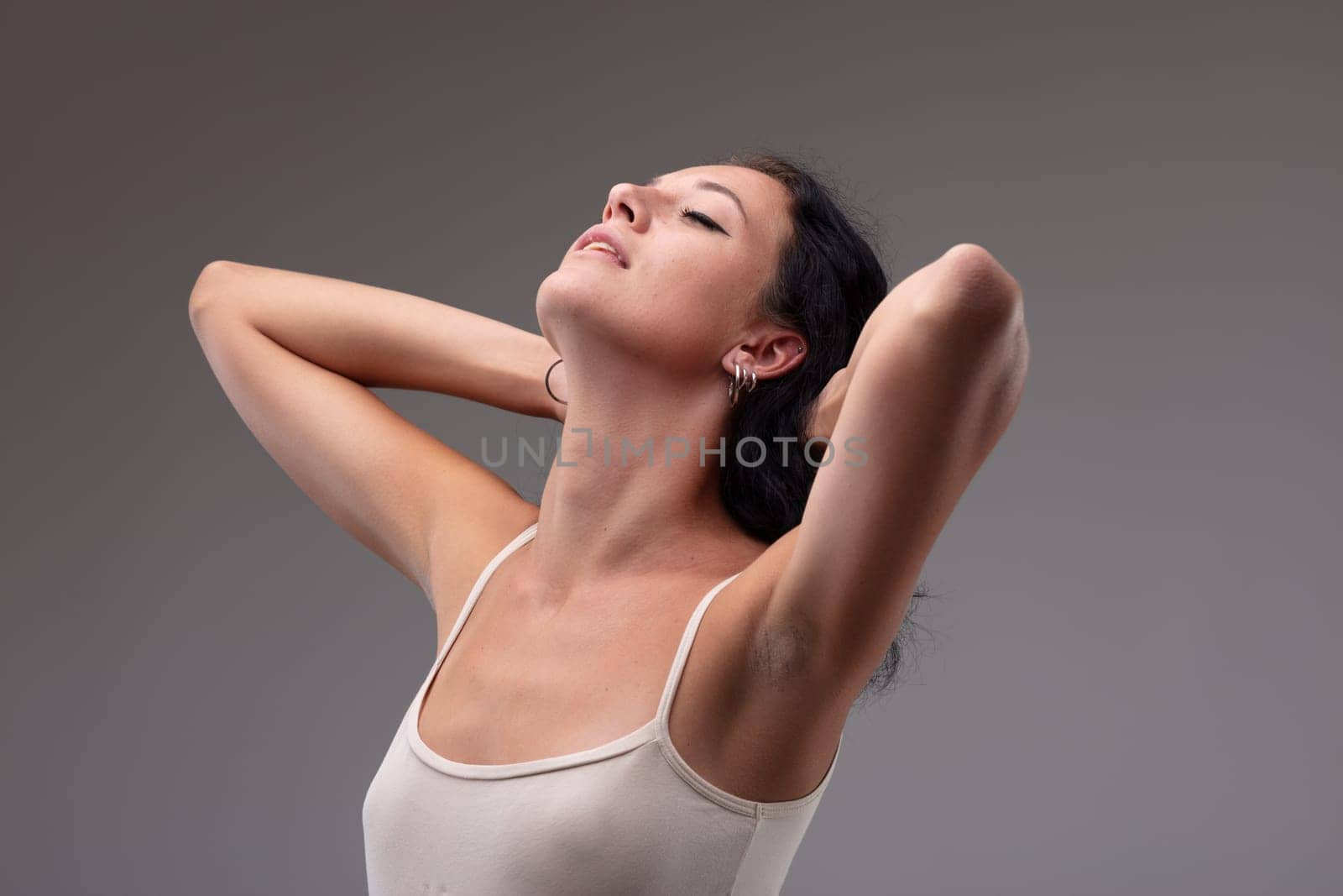 Serene young woman stretching back her head with parted lips and closed eyes with a blissful expression on a grey background