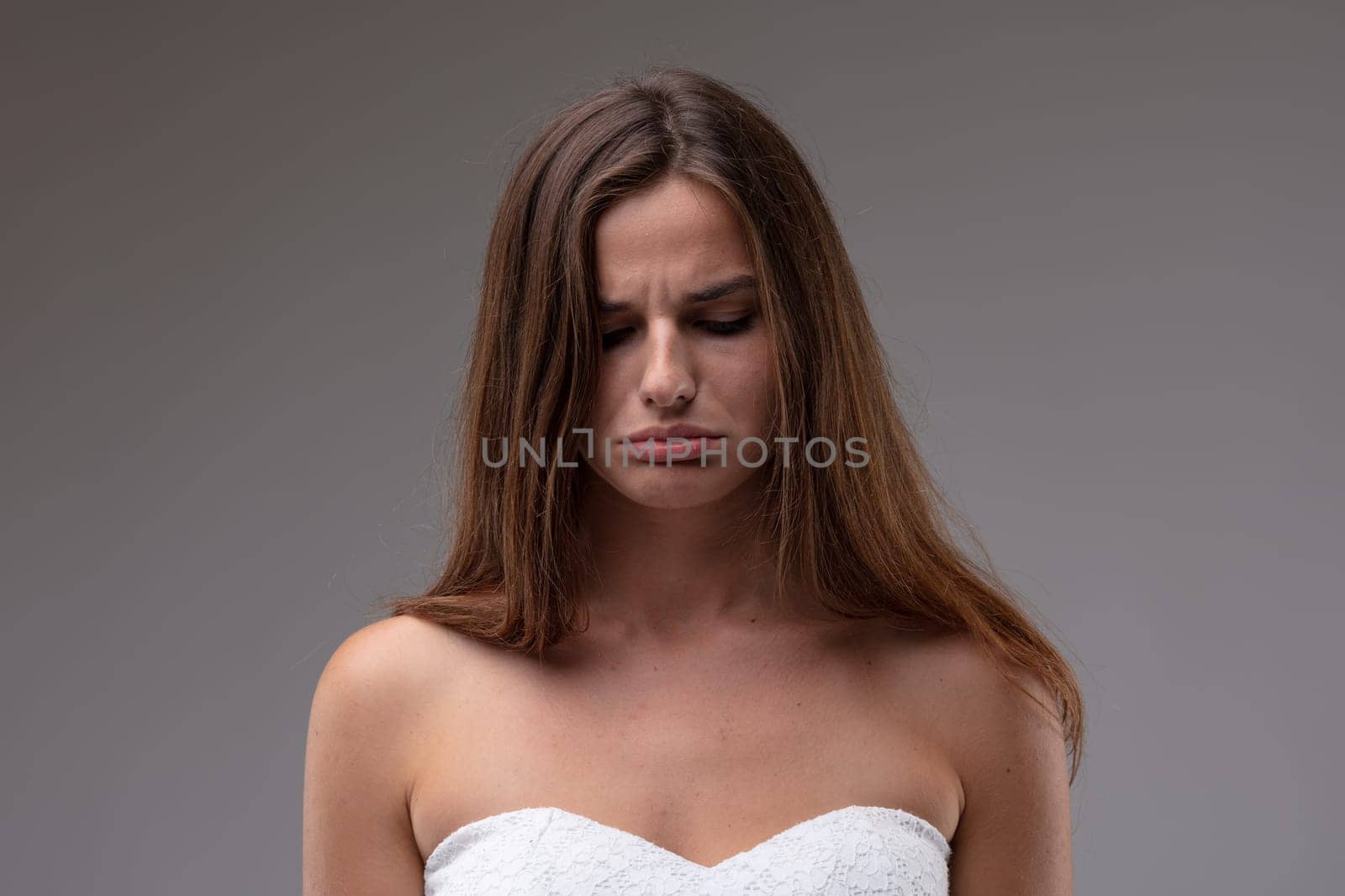 Sulky petulant attractive young woman scowling and pouting her lips in a close up head and shoulders portrait on a grey studio background