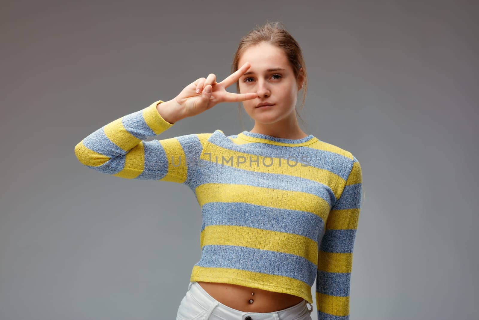 young woman in a fashion attitude, while making the V for victory, looks through us with a fascinating gesture