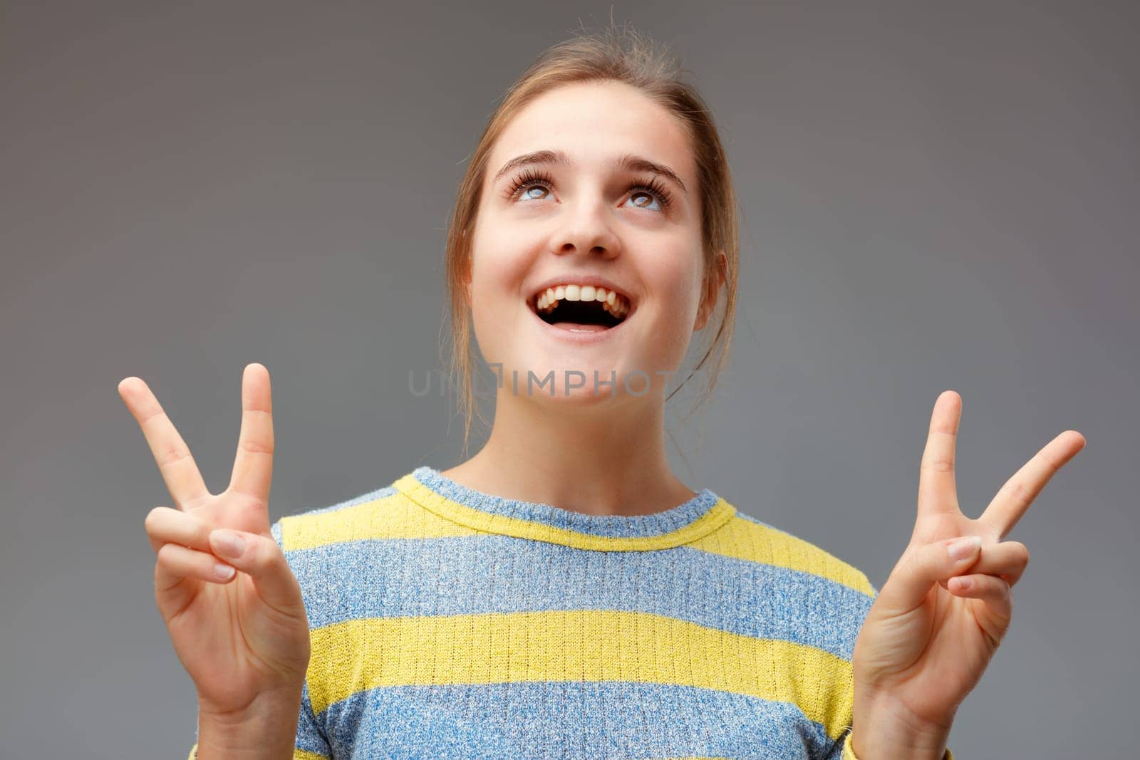 so lucky! young woman looks up to the sky, exclaiming for joy and making the V victory sign with both hands