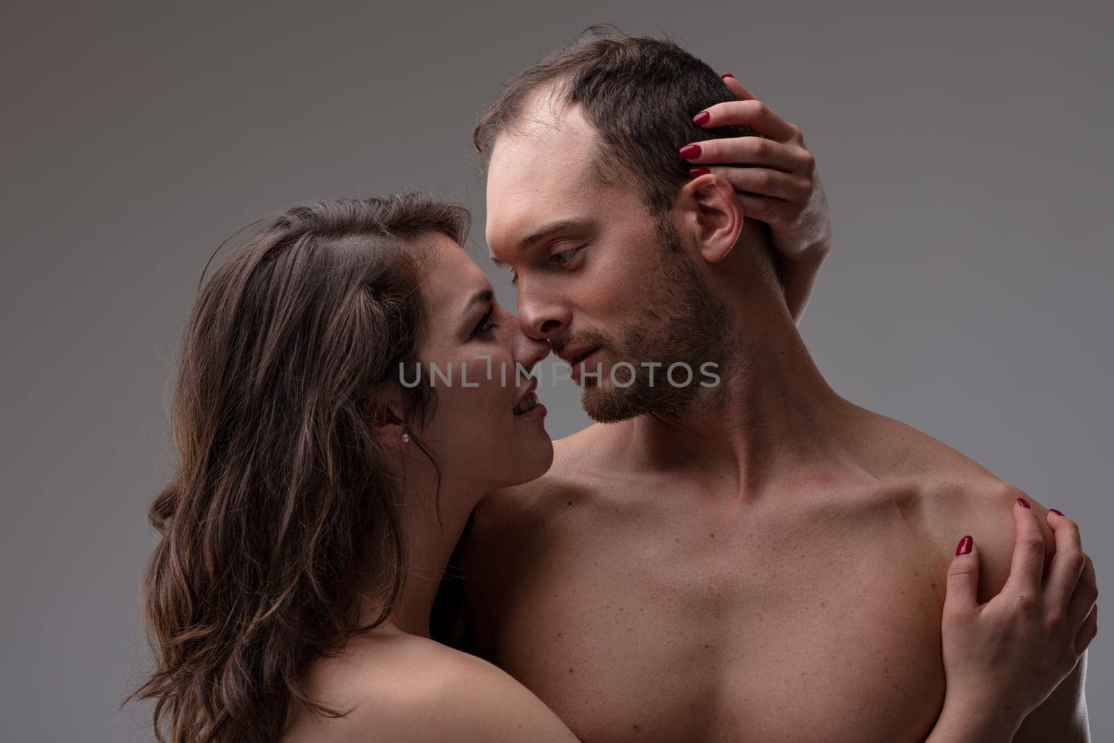 confident man and woman in love, she gently caresses the nape of his neck and brings him to her by touching the skin of his shoulder as their gazes cross in an infinite flow of love