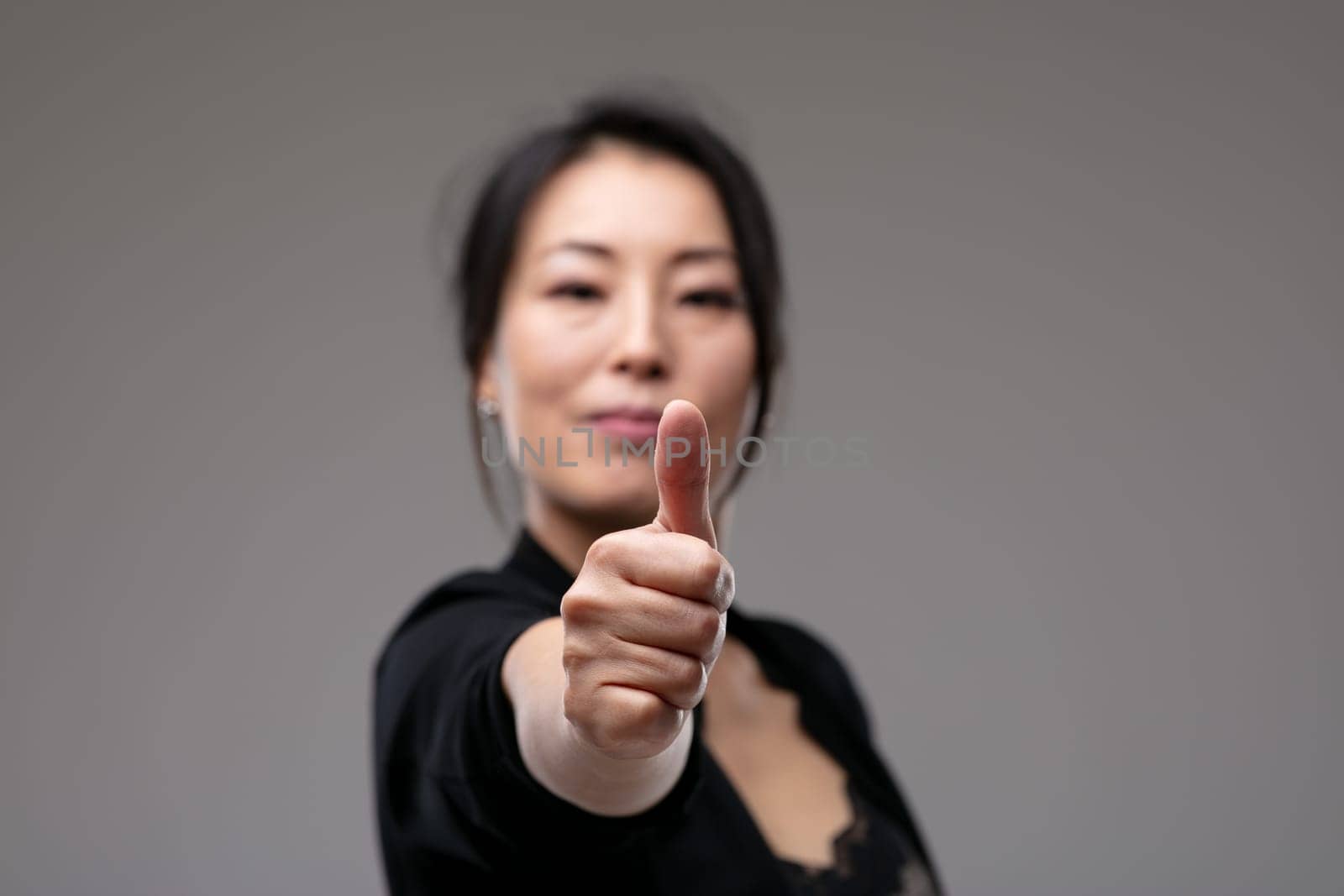 Successful motivated woman giving a thumbs up gesture with a quiet pleased smile of achievement over a grey studio background with copyspace