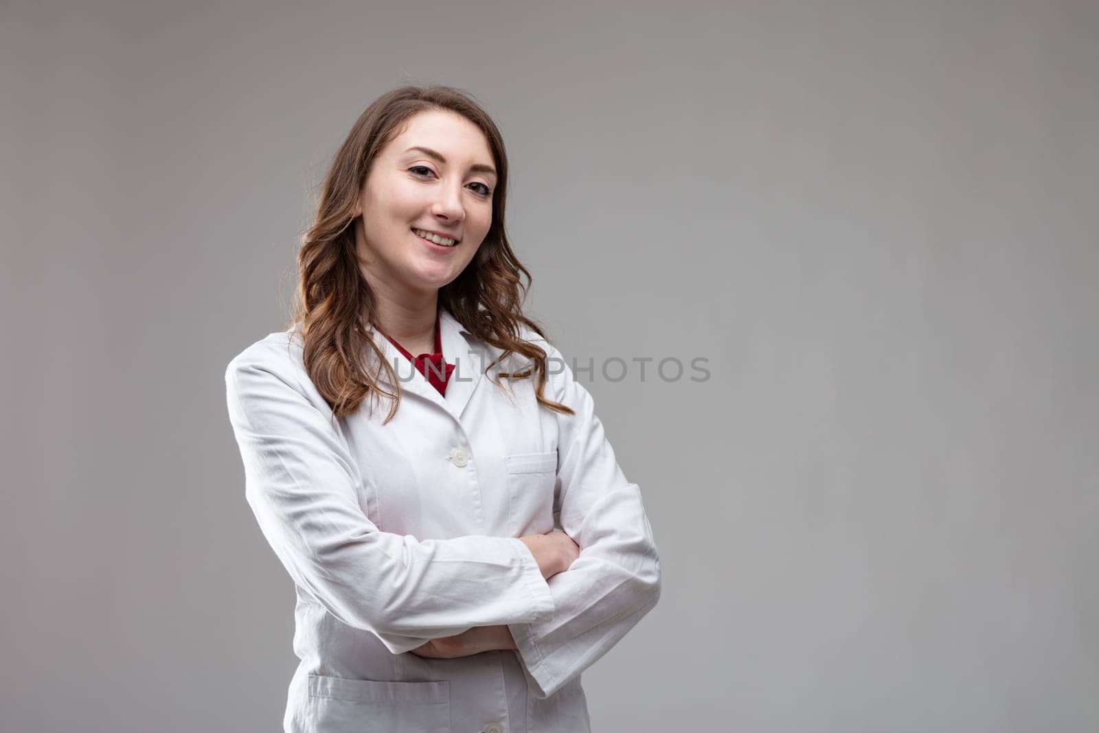 Confident friendly woman doctor or nurse in a lab coat standing with folded arms smiling at the camera on a grey background