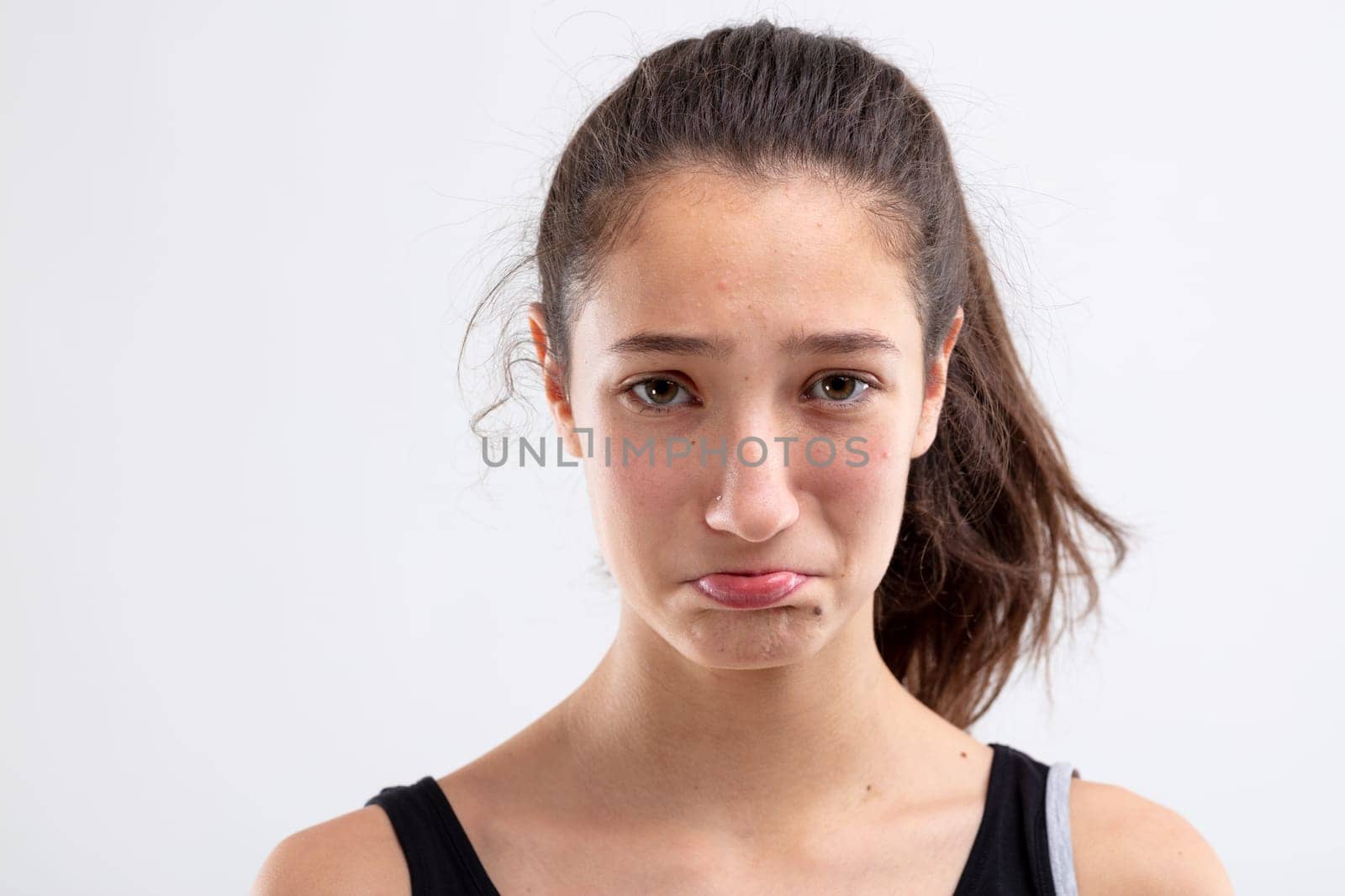Sulky miserable young woman pouting her lips and looking at the camera with sorrowful eyes in a close up head shot on white