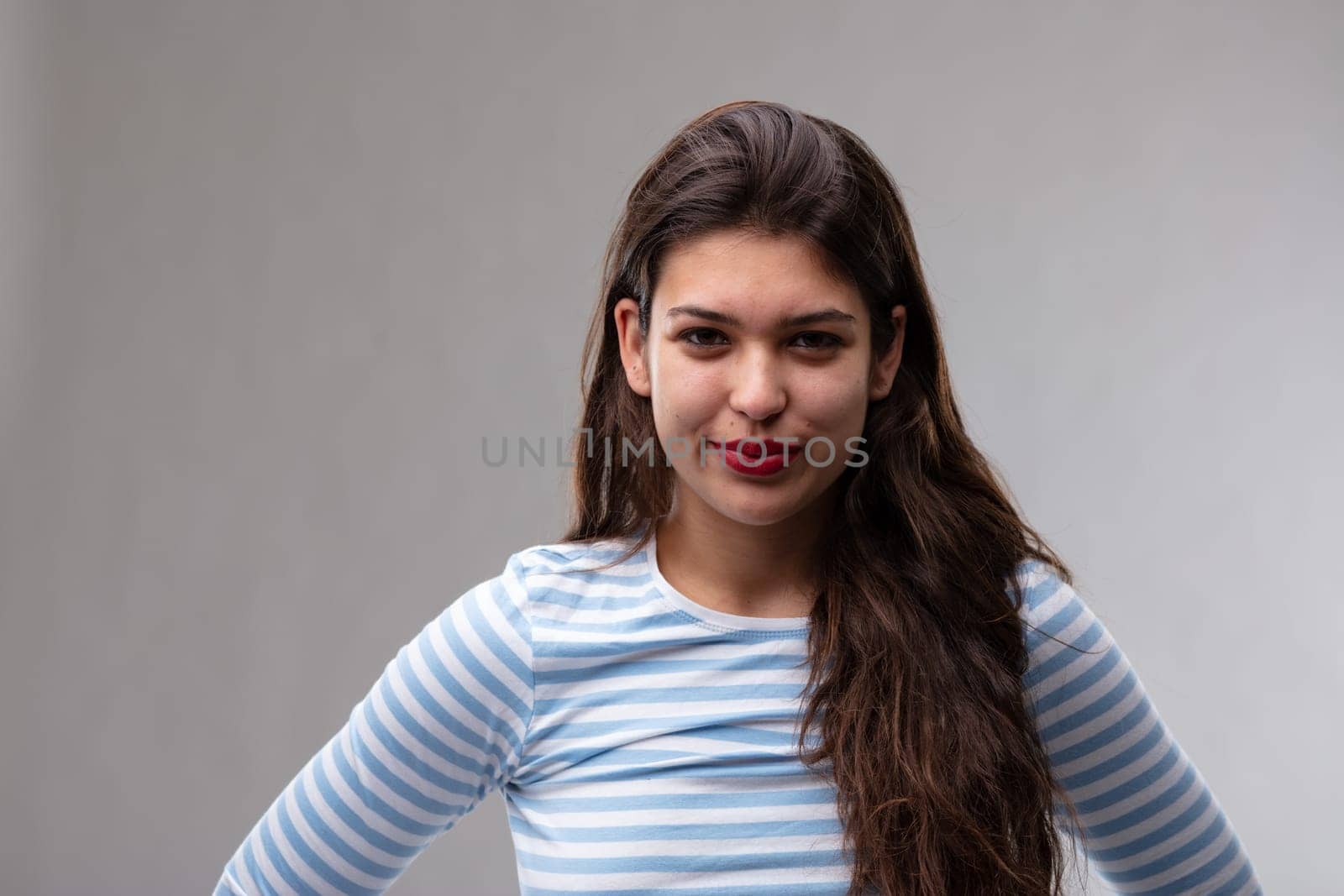 Amused attractive dark haired young woman grinning at the camera with laughing eyes over a grey studio background