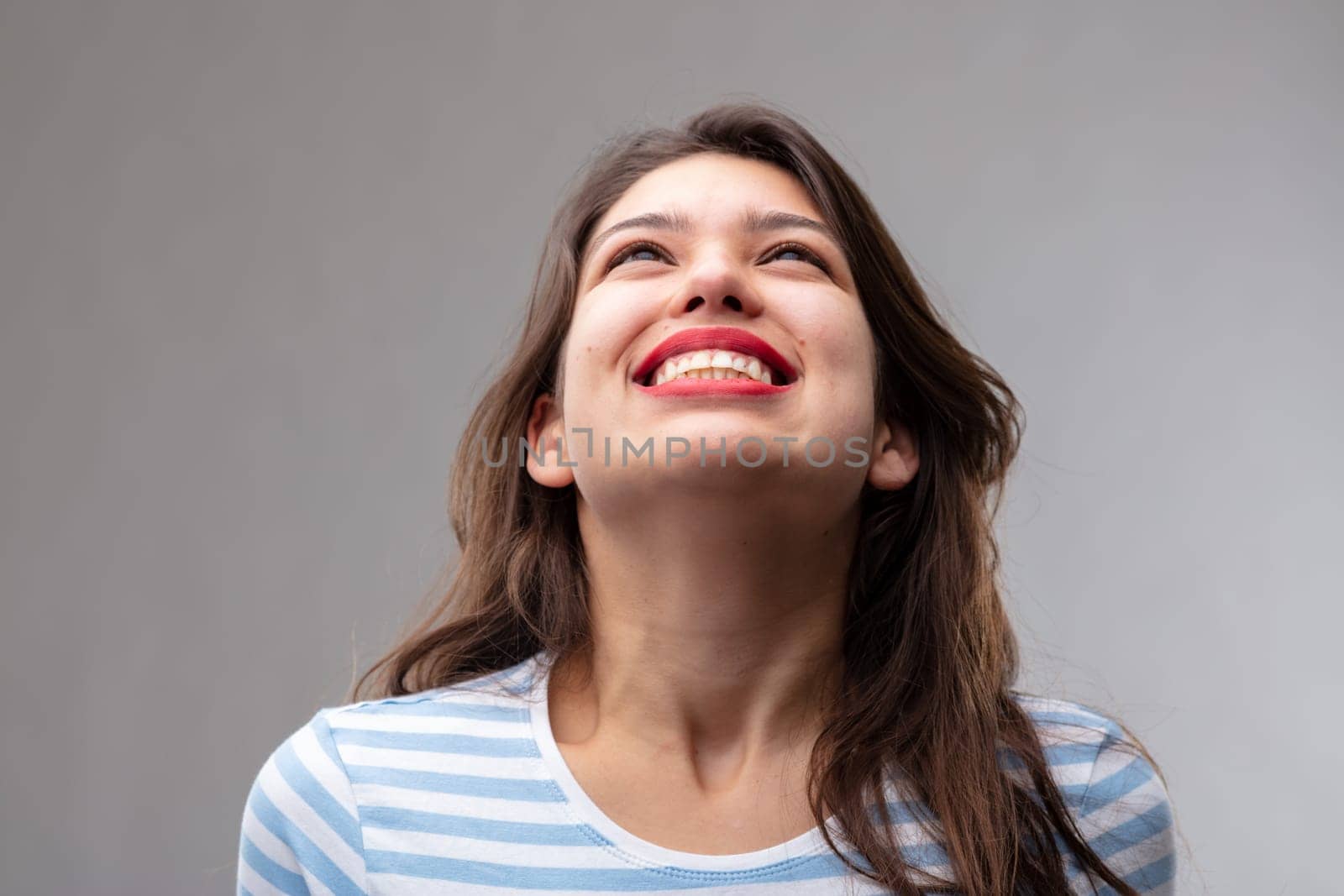 Happy carefree young woman with a joyful smile looking up smiling with pleasure and excitement over a grey studio background
