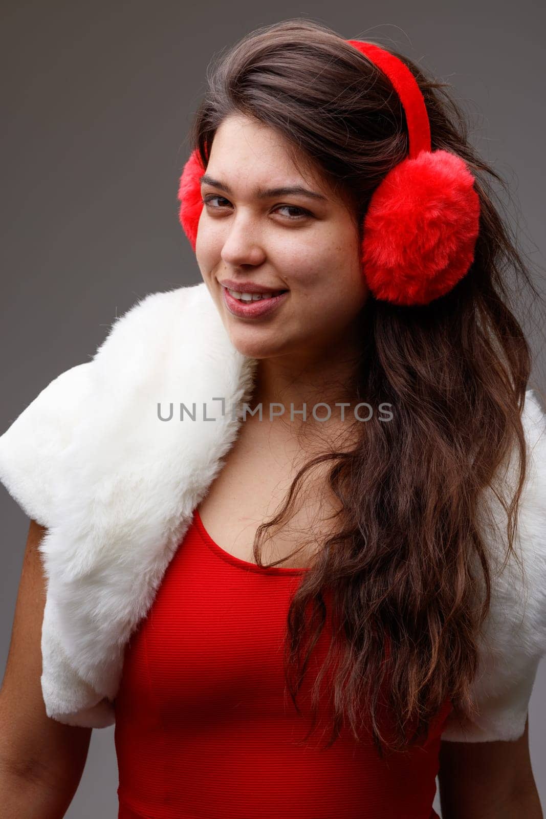 Attractive young woman wearing colorful red ear muffs and top with an elegant fluffy white jacket conceptual of Christmas and the festive winter season