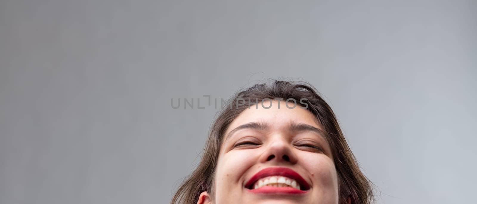 Panorama banner of a joyful young woman with her head thrown back and a beaming smile in a close up cropped portrait over a grey studio background with copy space