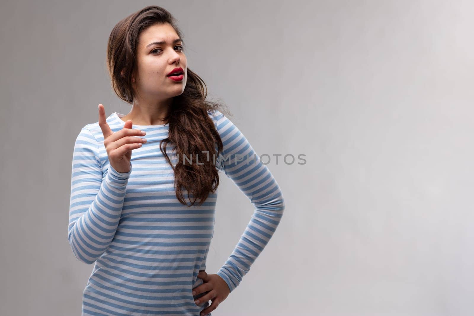 Young dogmatic woman having a serious discussion wagging her finger to make a point as she looks sideways at the camera over a grey studio background with copy space