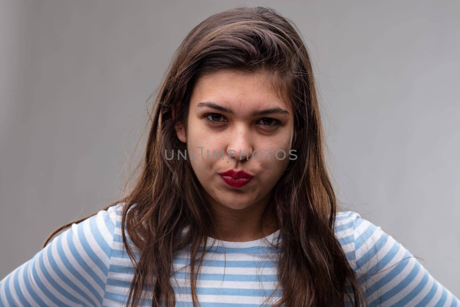 Angry young woman pursing her lips and giving the camera a baleful glare with an intense expression over a grey studio background