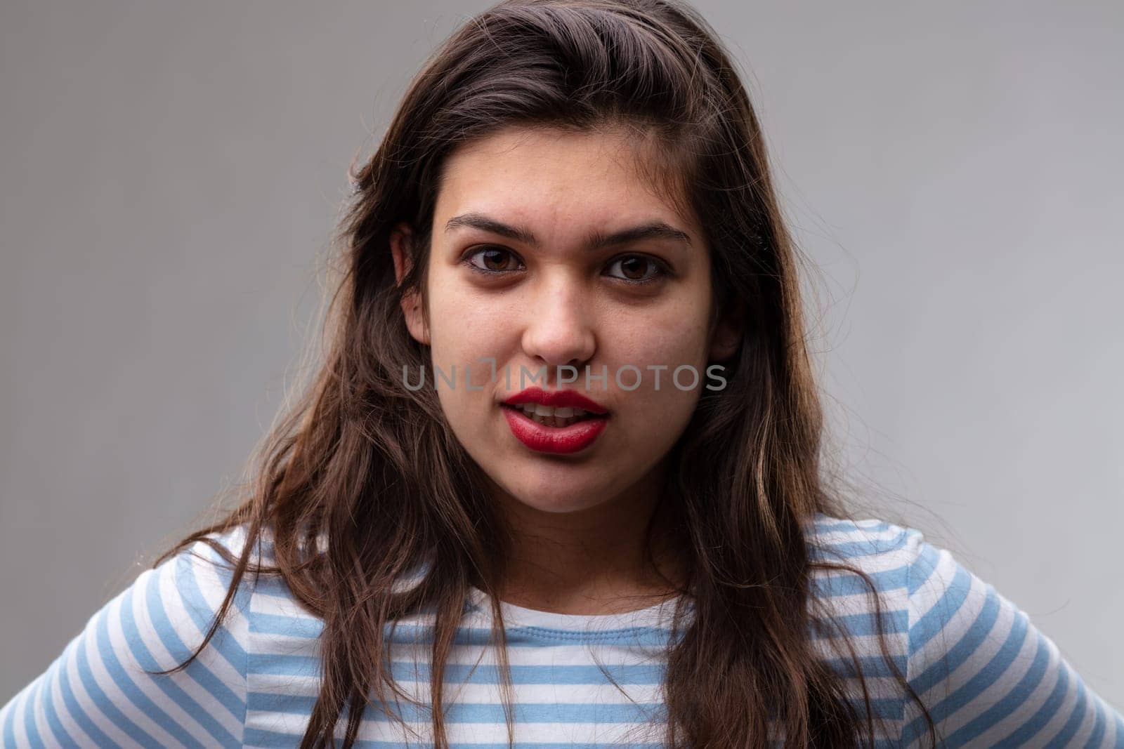 Serious young woman with a penetrating stare looking directly into the camera with parted lips and a pensive expression over a grey studio background