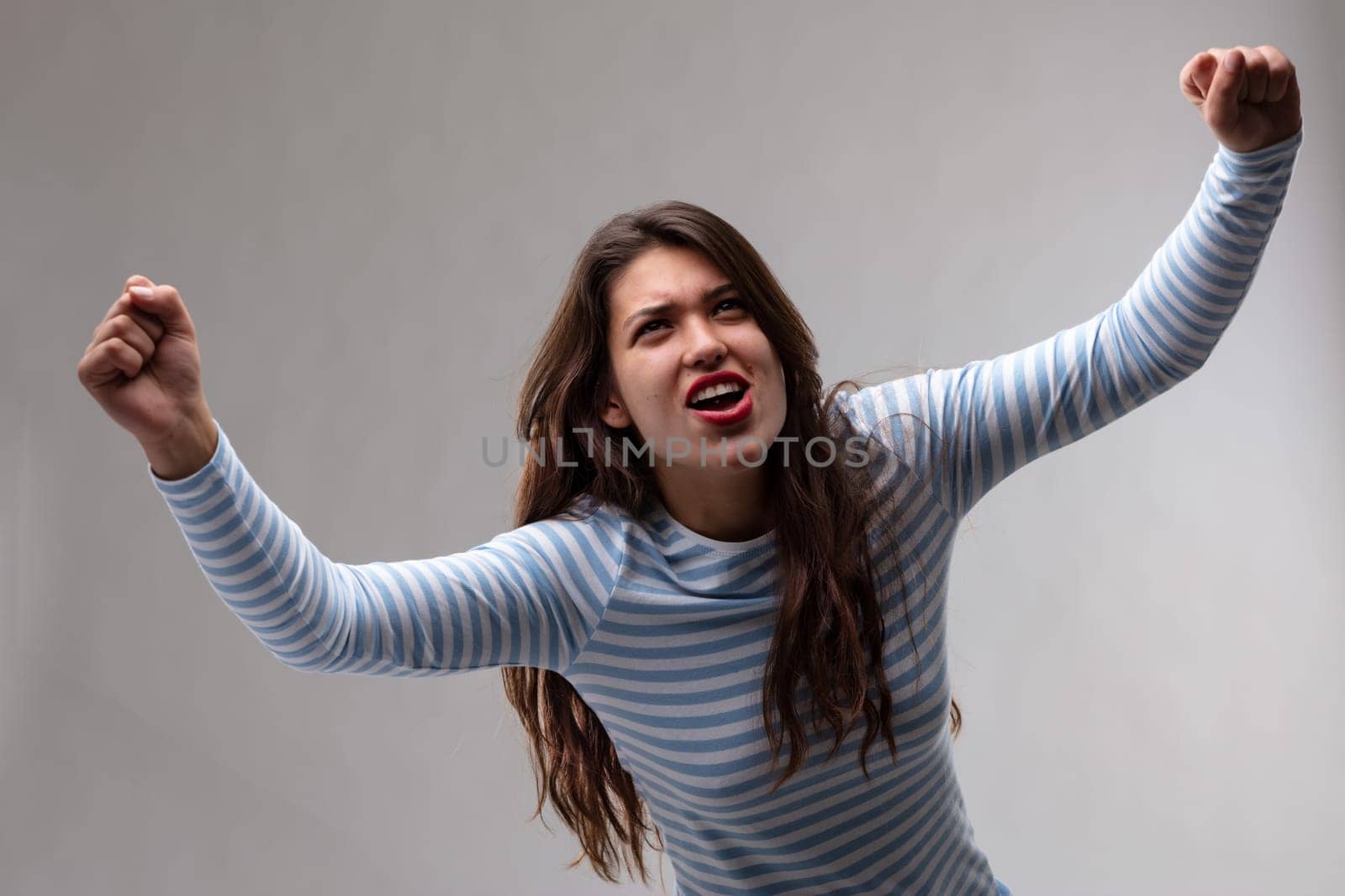 Victorious exultant young woman cheering and punching the air with her fists in a high angle view over a grey background