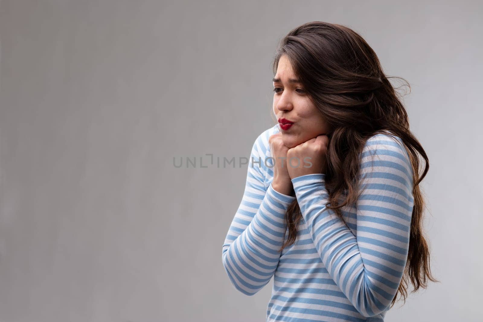 Young woman with a passionate crush or fancy holding her fists to the throat with pursing her lips over a grey background with copy space
