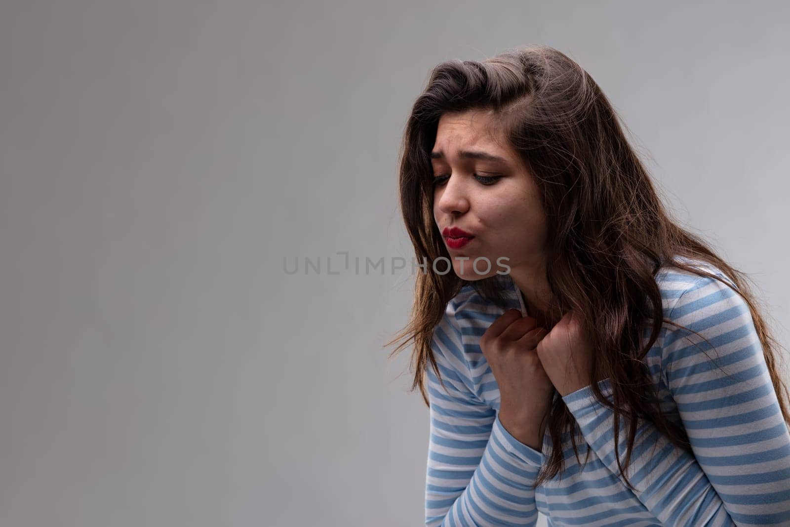 Young woman with a passionate craving or yearning holding her hands to her throat as she bends forwards pouting over a grey background with copy space