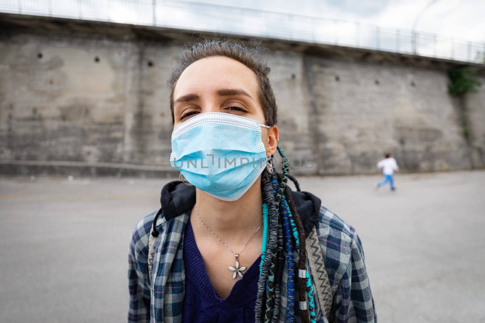 portrait of a young rebellious woman with rasta hairstyle in an urban setting wearing a protective mask covering her face and letting see her eyes facing adversity