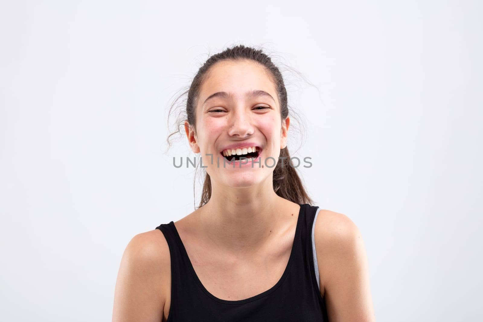 Laughing vivacious happy young woman with her long hair tied back in a pony tail in a head and shoulders studio portrait