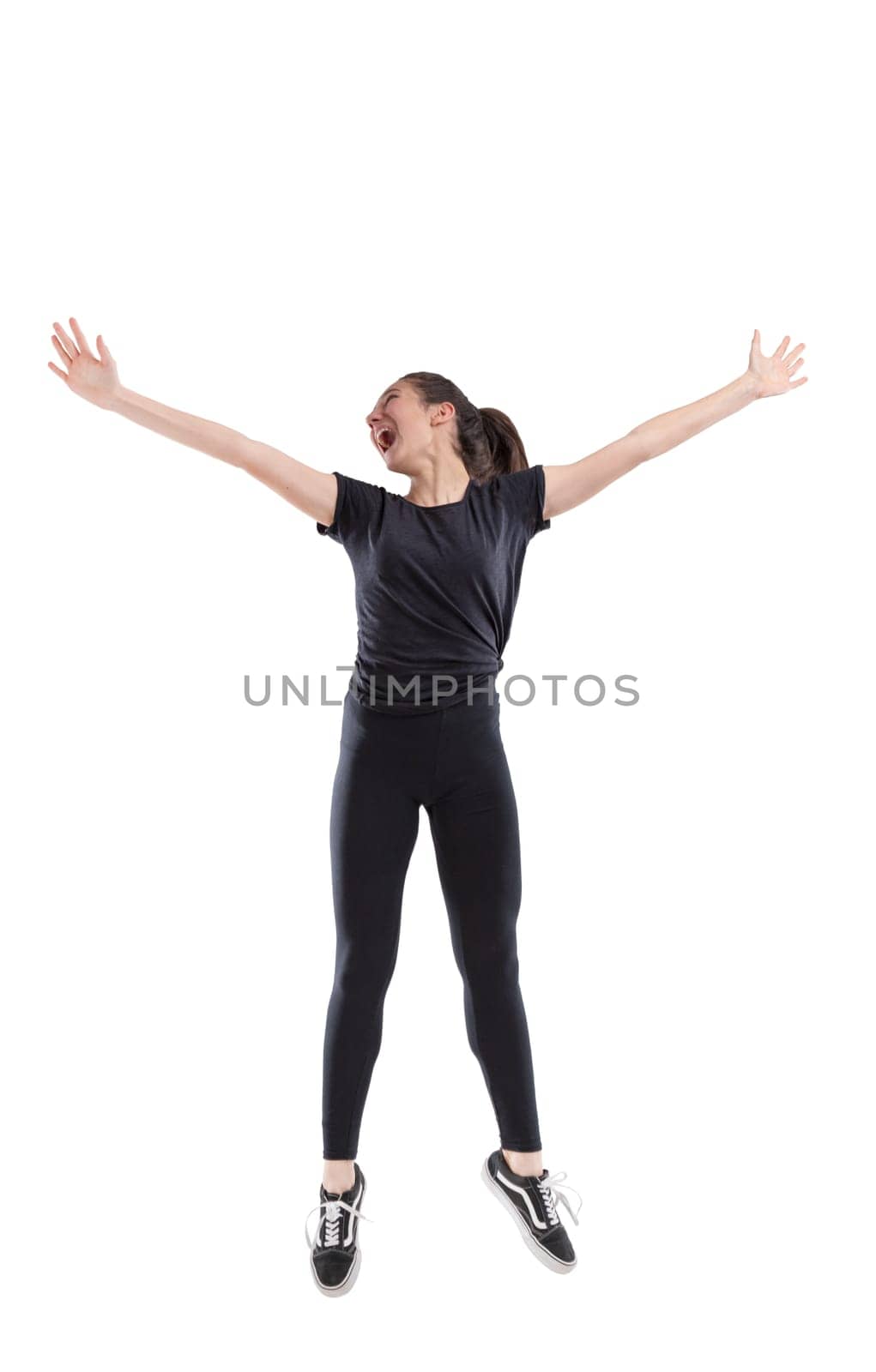 Exuberant laughing vivacious young woman jumping for joy with outstretched arms isolated full length on white