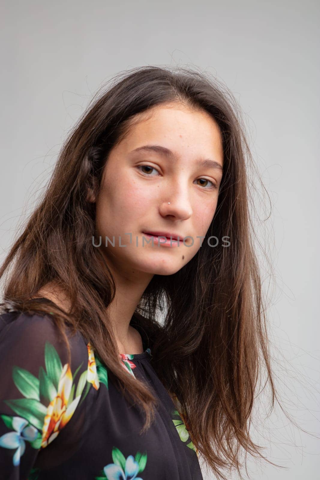 Thoughtful young woman looking quietly at camera in a half turned head portrait over grey