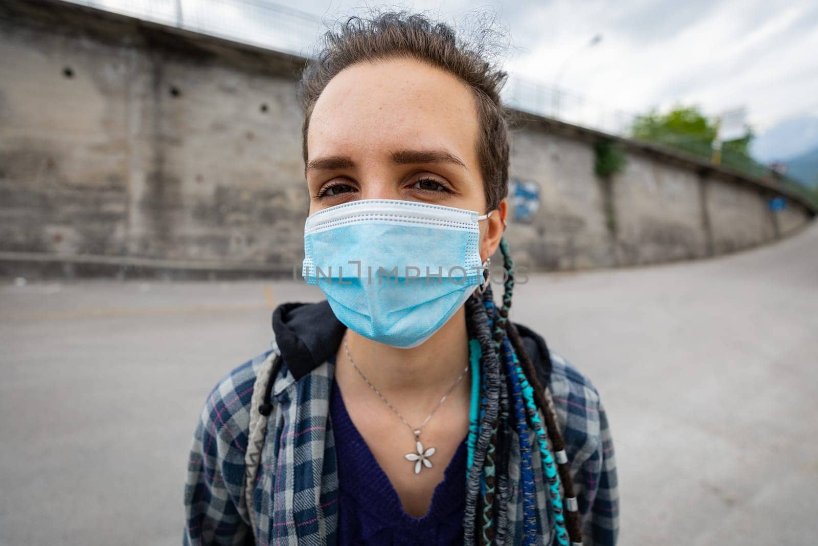 portrait of a young rebellious woman with rasta hairstyle in an urban setting wearing a protective mask covering her face and letting see her eyes facing adversity