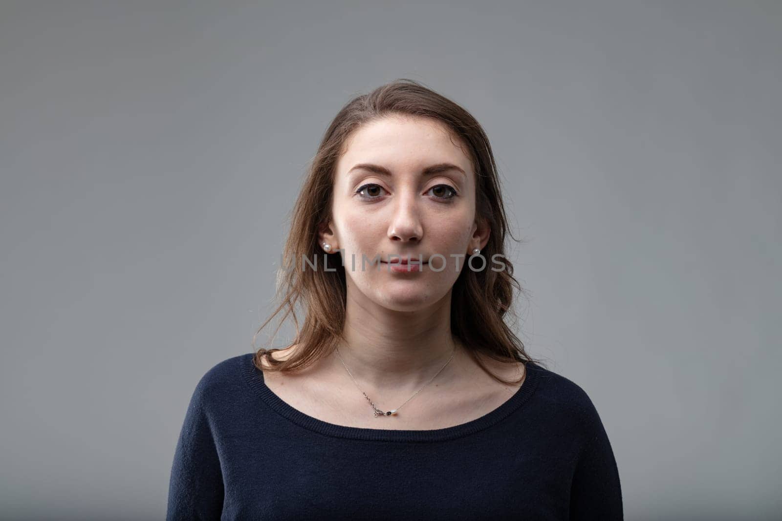 Serious attractive middle-aged woman with shoulder length hair wearing a black top over a grey background