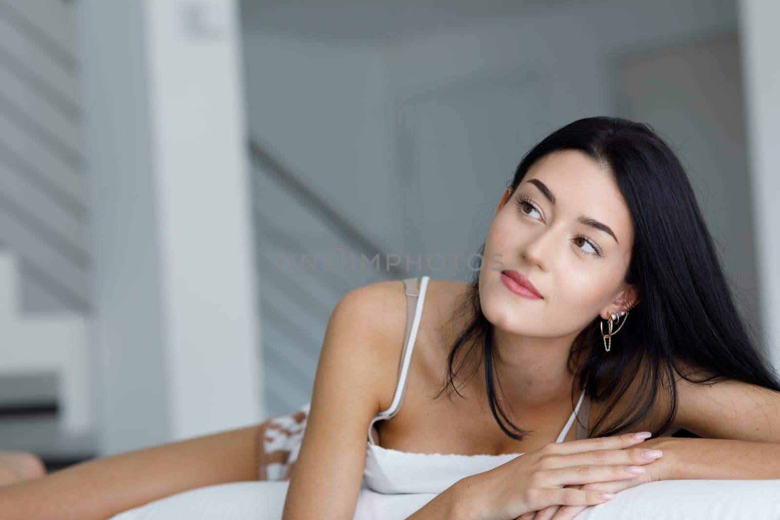 Young woman lying daydreaming or thinking over her aspirations lying relaxing on a sofa in leisurewear looking to the side with a faraway expression