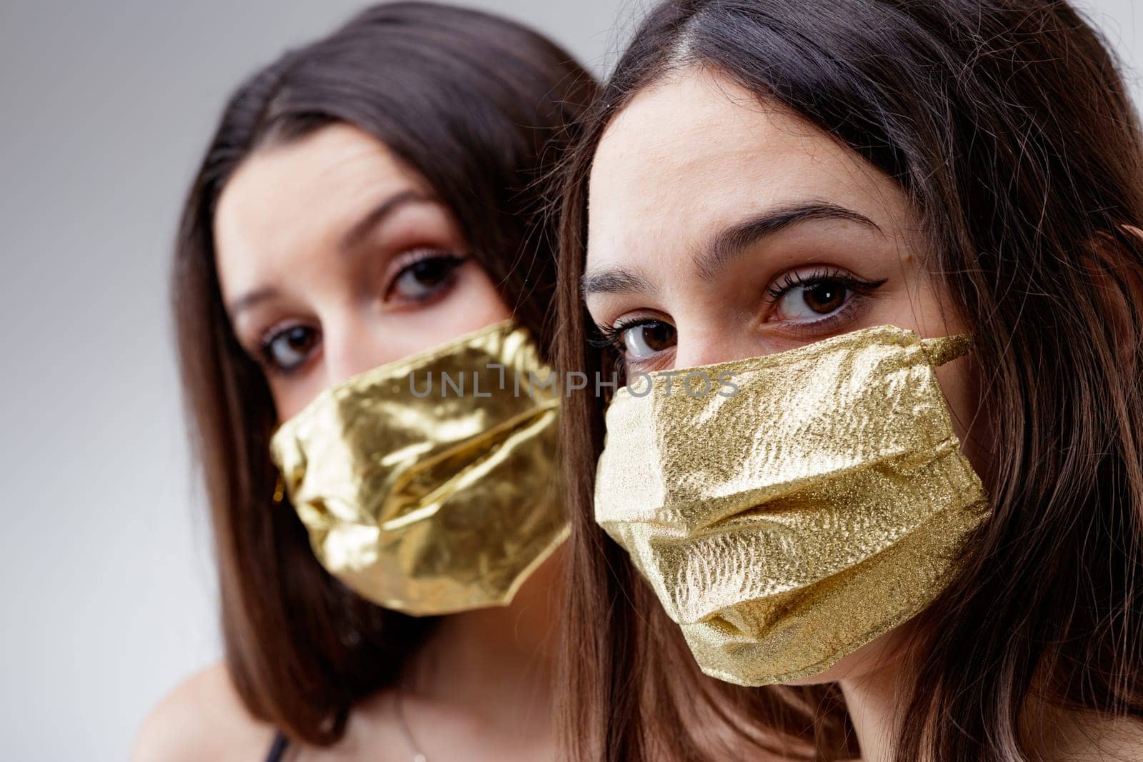 women wearing GOLDEN protective face masks watching you, young woman good looking and lucky in golden facial covers protect from COVID-19 coronavirus on a neutral babkcround, affordable healthcare concept