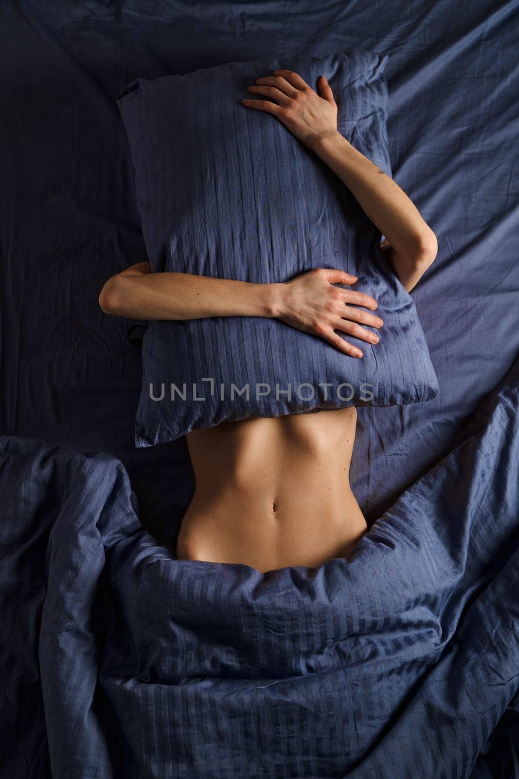 Concept of social phobia and panic attack. Woman hides her face with pillow while lying in bed.