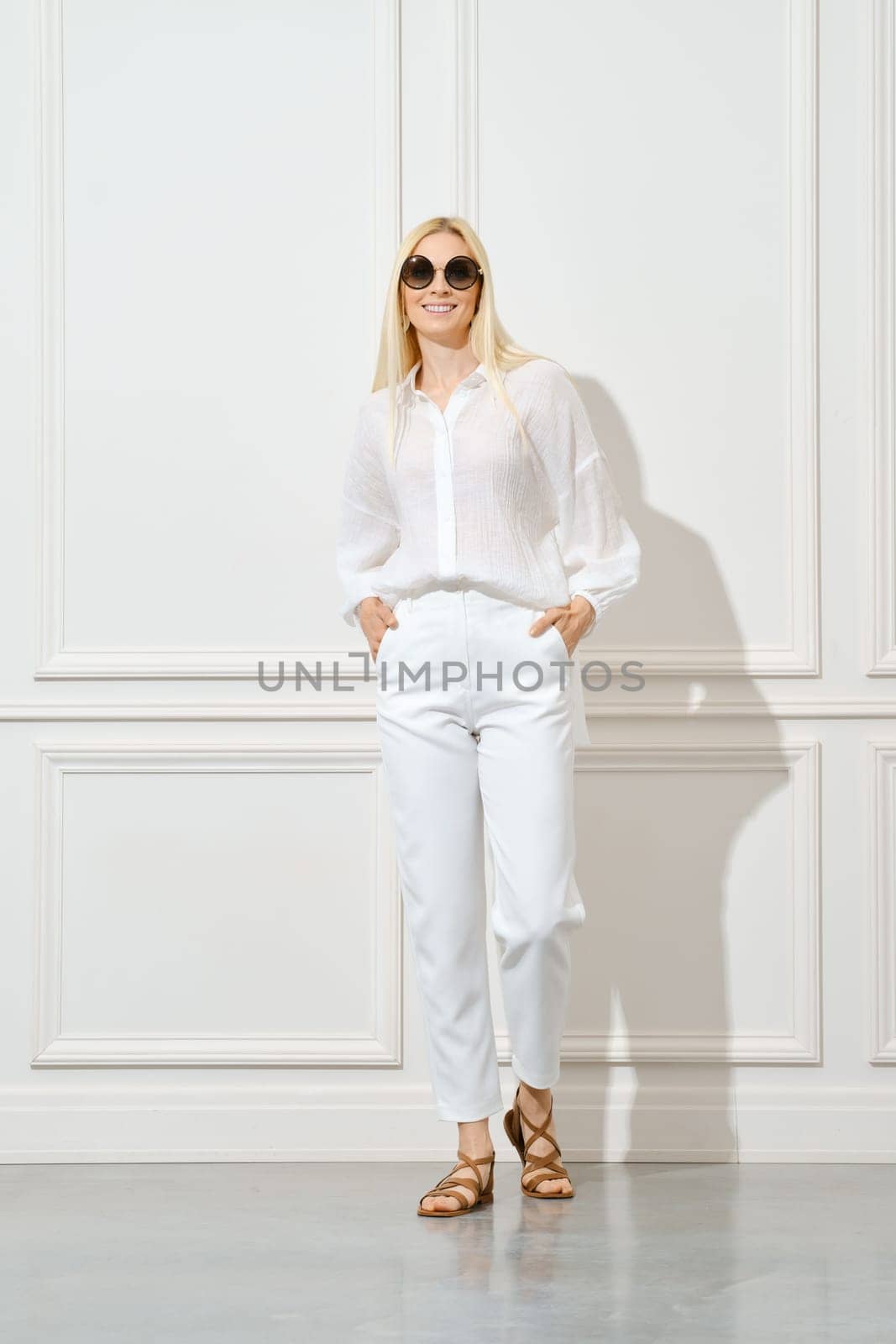 Cheerful woman in white cotton shirt, sunglasses and trousers posing indoors
