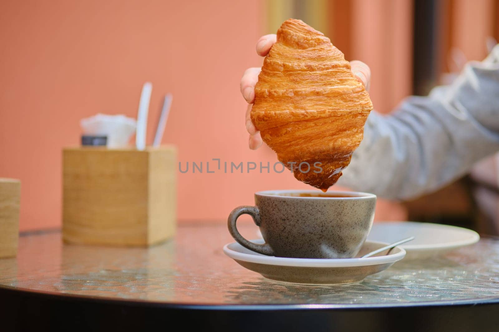 Unrecognizable woman dipping croissant into cappuccino on outdoor terrace