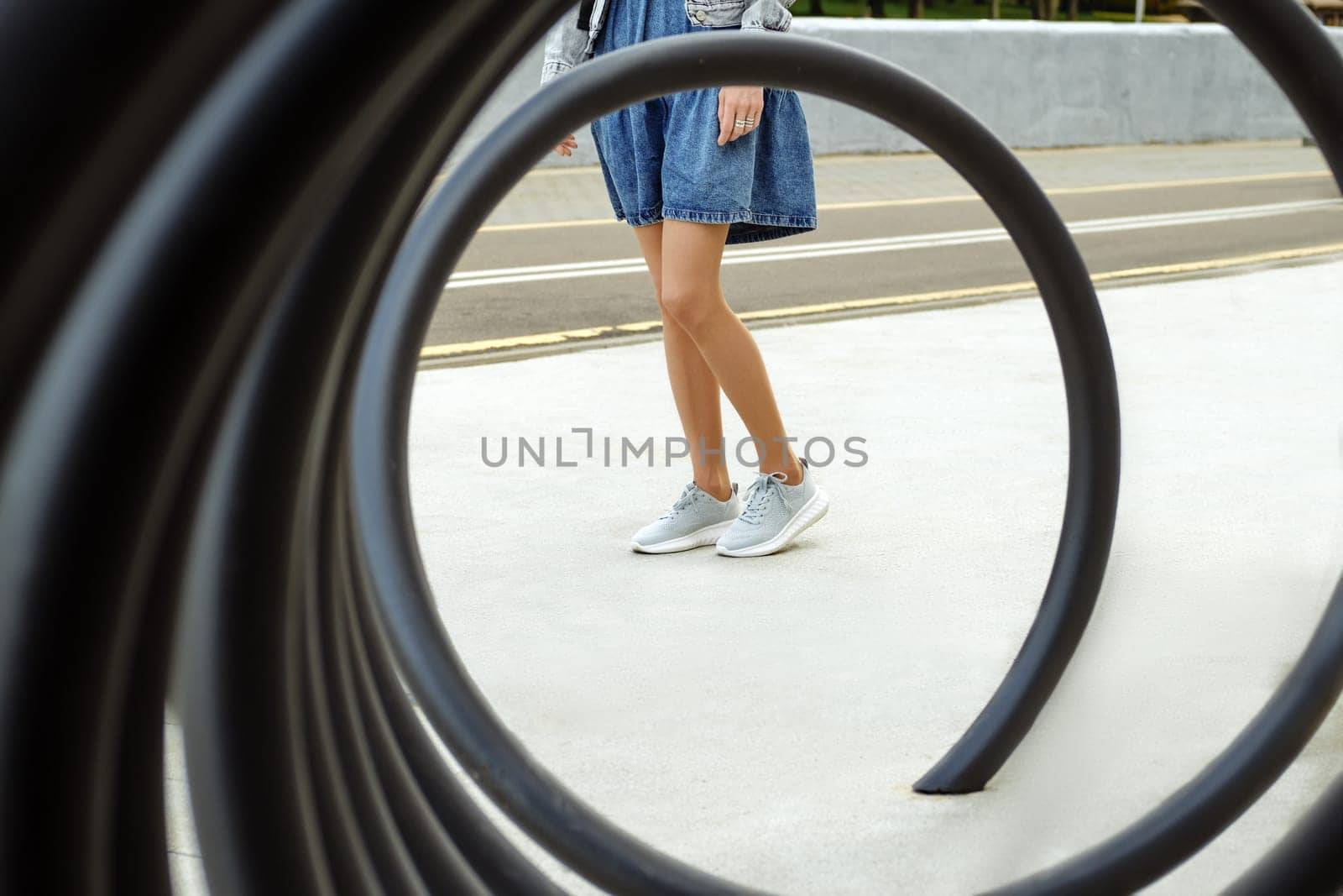 View through metal spiral on legs of unrecognizable woman in beige tights and sneakers