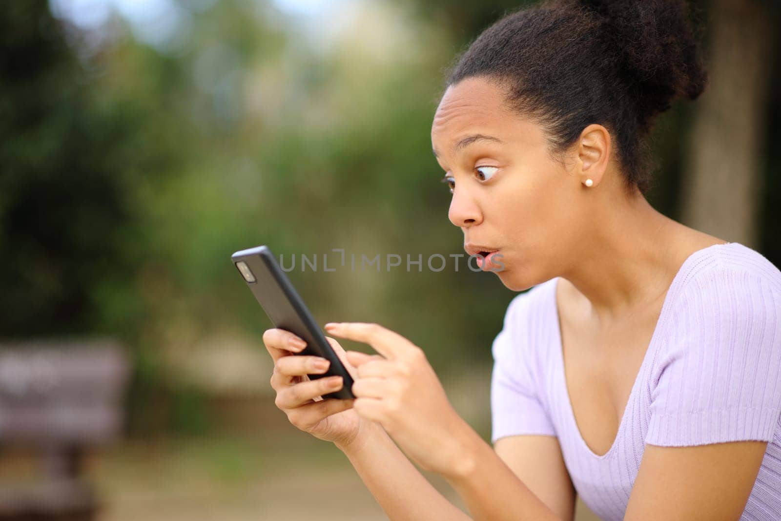 Amazed black woman checking phone content in a park