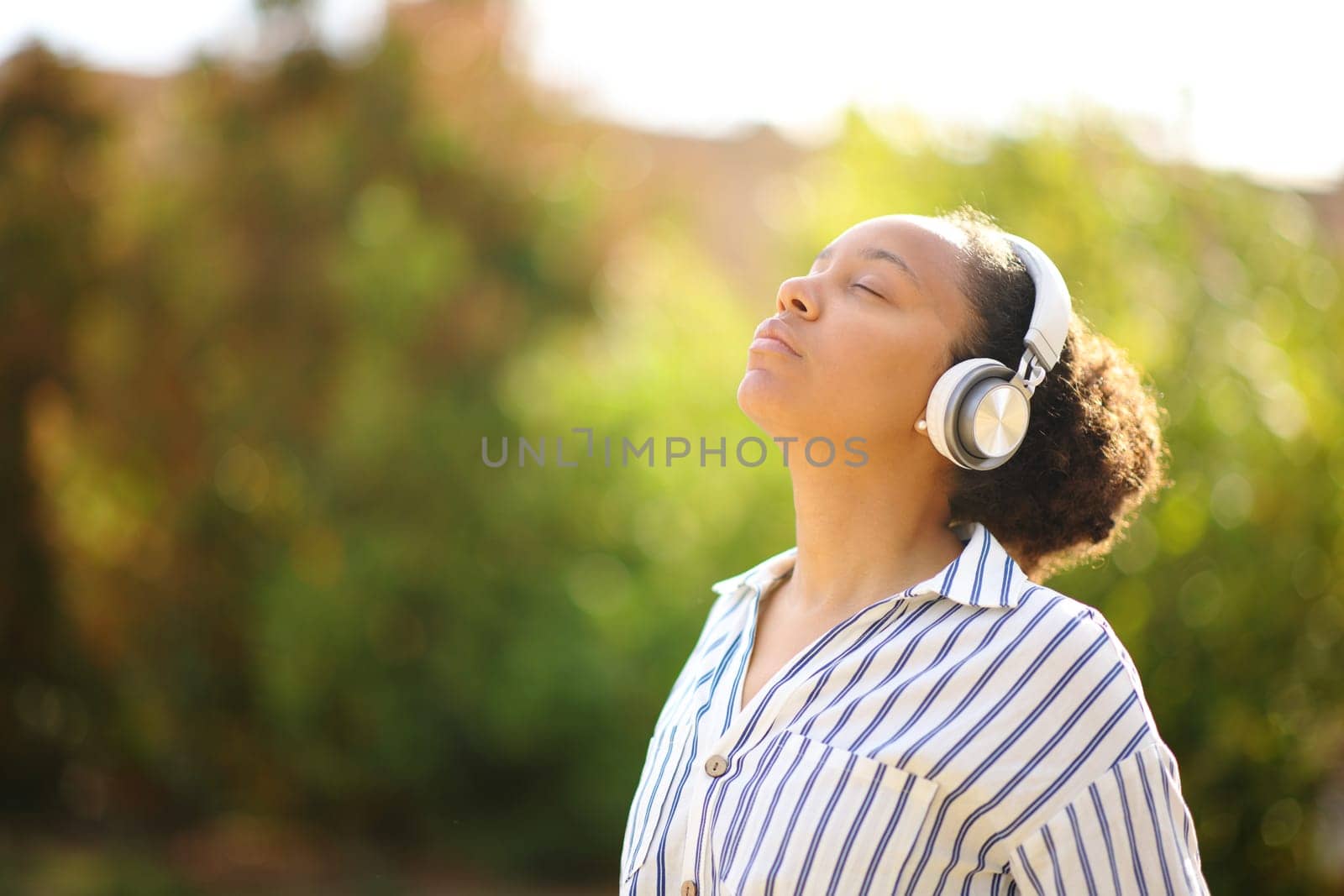 Black woman meditating using headphone in a park