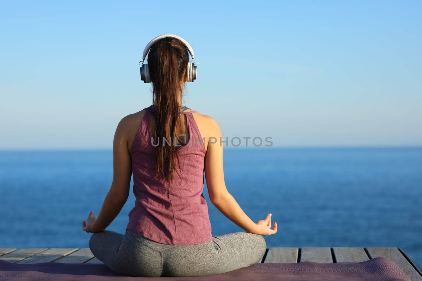 Back view of a yogi doing yoga with headphone on the beach