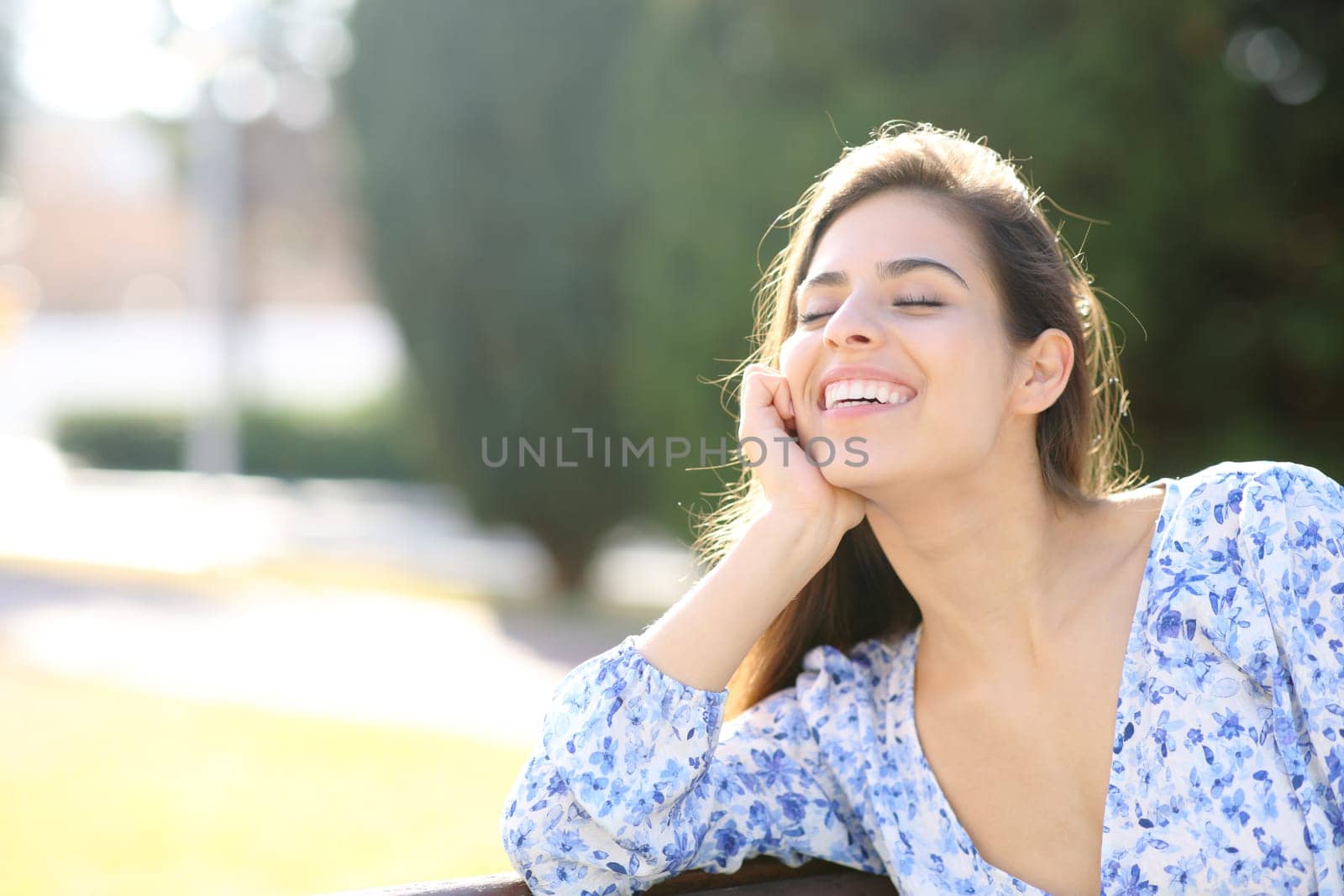 Happy woman laughing sitting on a bench in a park