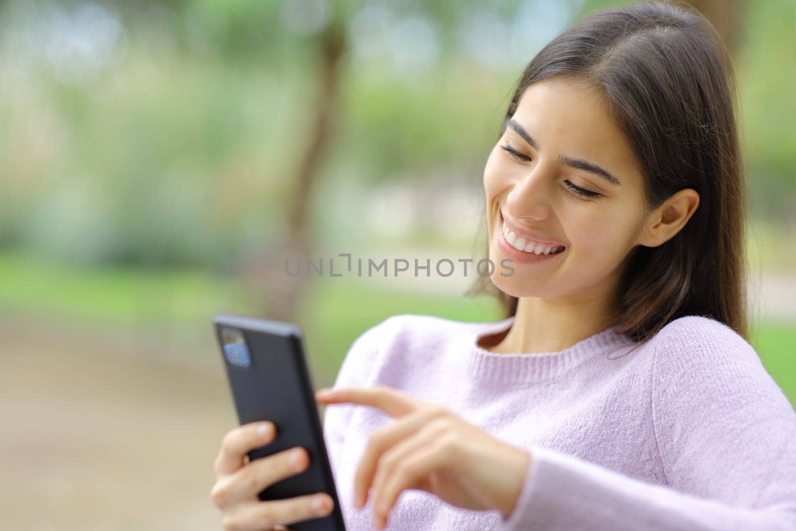 Happy woman is using cell phone sitting in a park