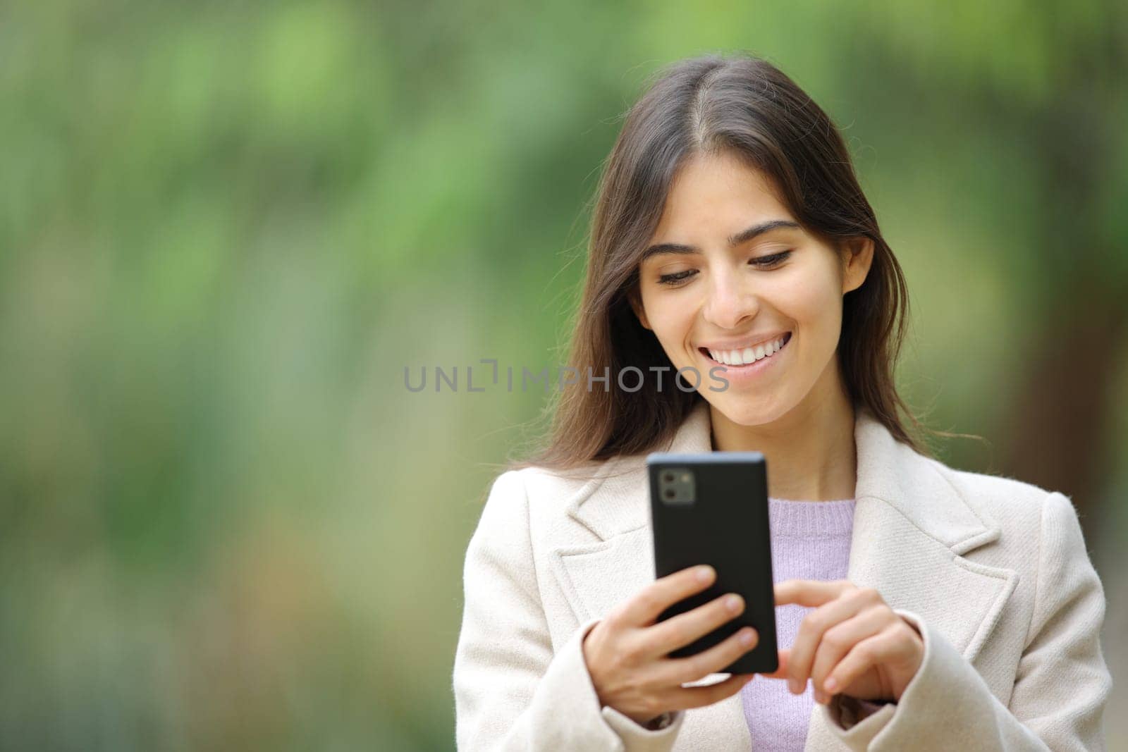 Front view portrait of a happy woman walking using cell phone in winter