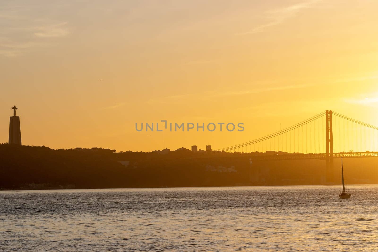 Orange sunset over the Tagus River - the statue of Jesus christ and the bridge over the river. Mid shot