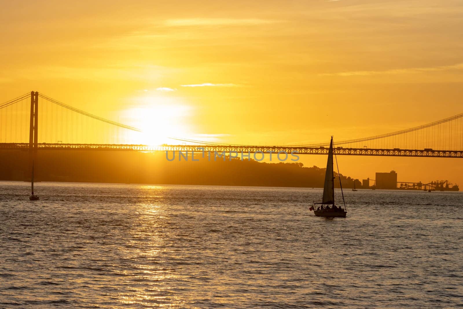 Bright orange sunset over the river and a sailing boat floating towards the bridge. Mid shot