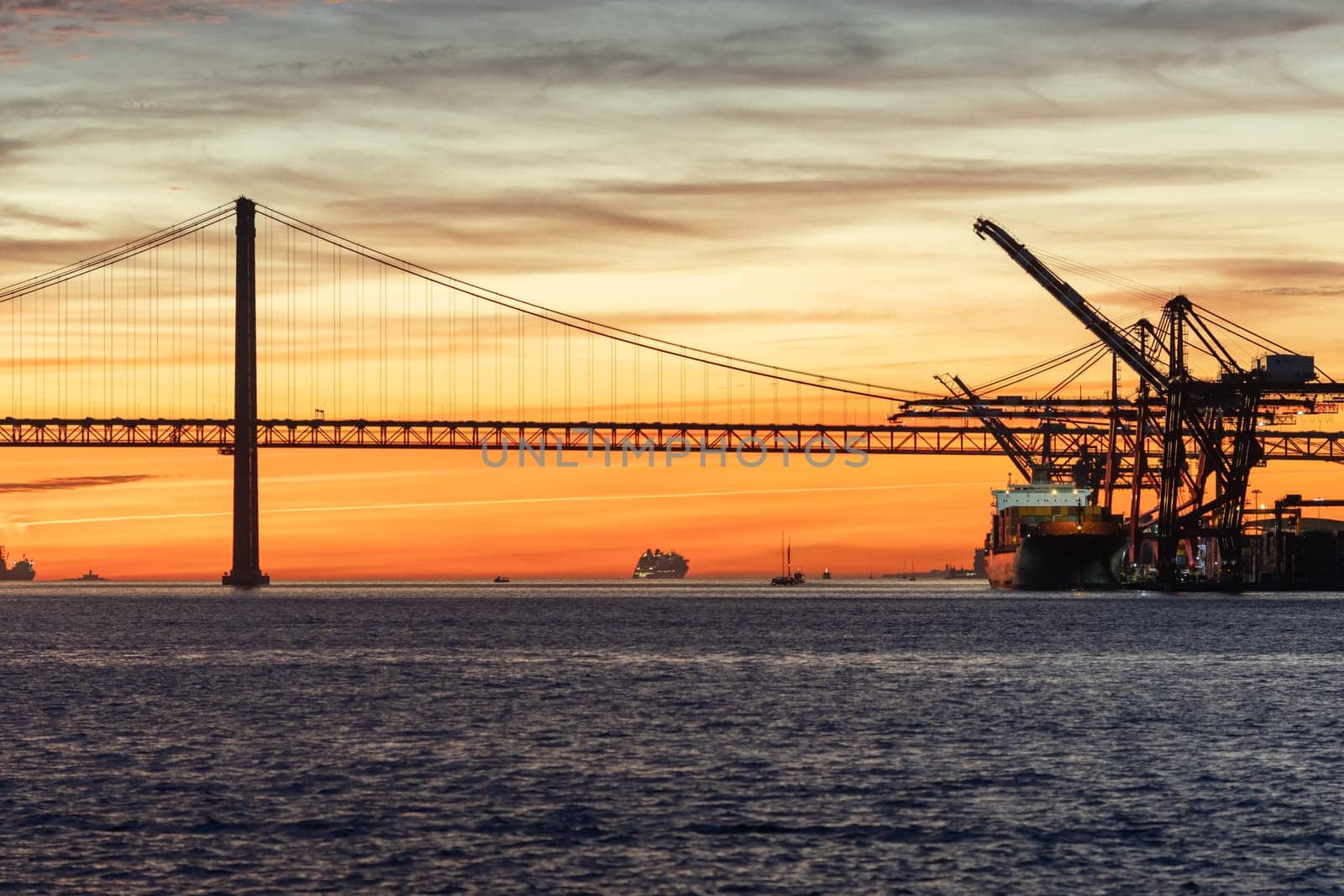 Lisbon and 25th of April Bridge at sunset - industrial cranes working by the water. Mid shot