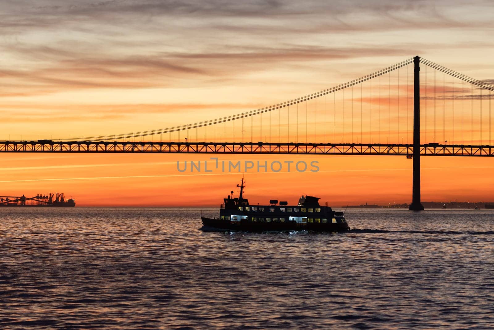 Lisbon and 25th of April Bridge at sunset - the transport ship sails on the Tagus River. Mid shot