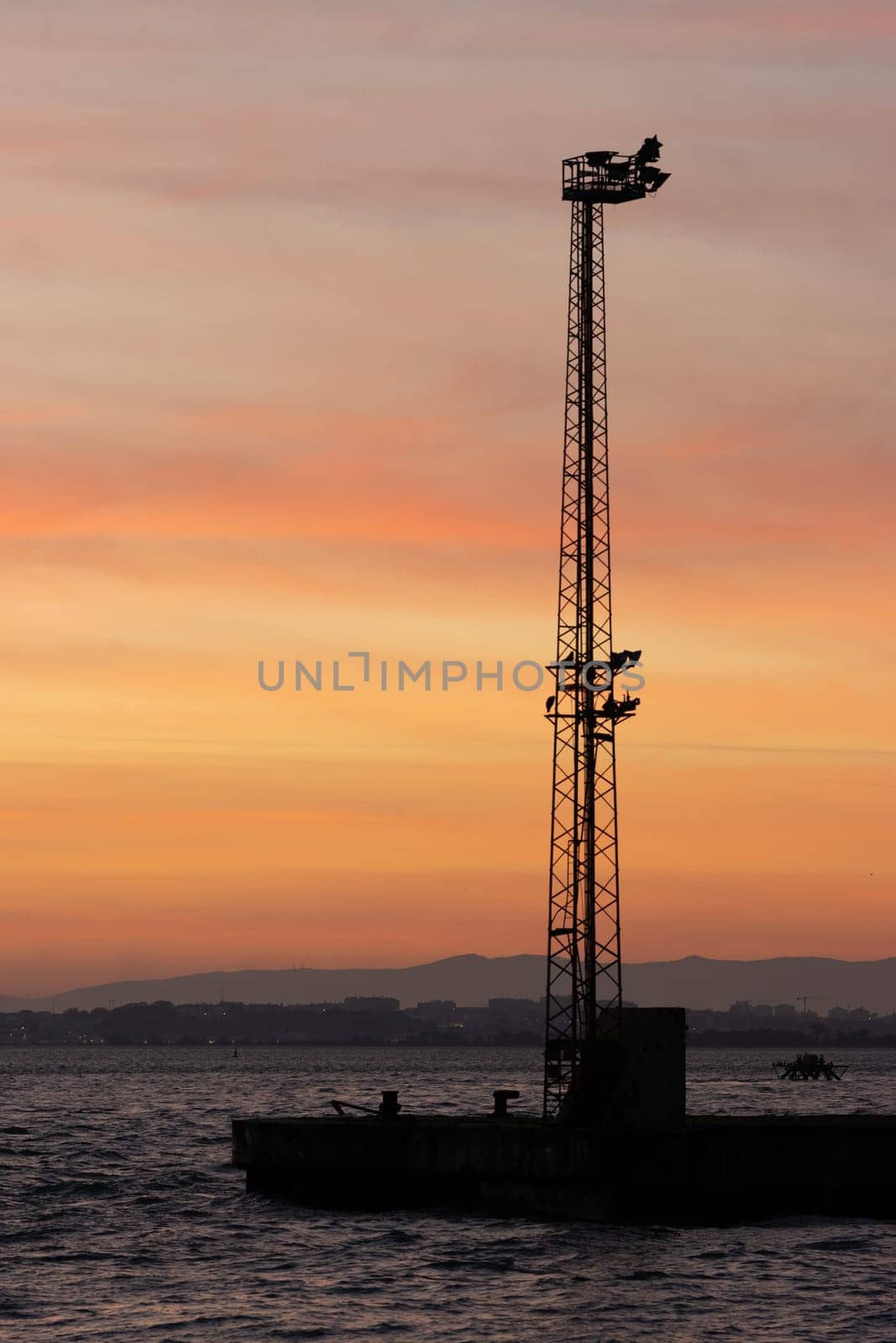 Electric tower on the water at an orange sunset. Mid shot