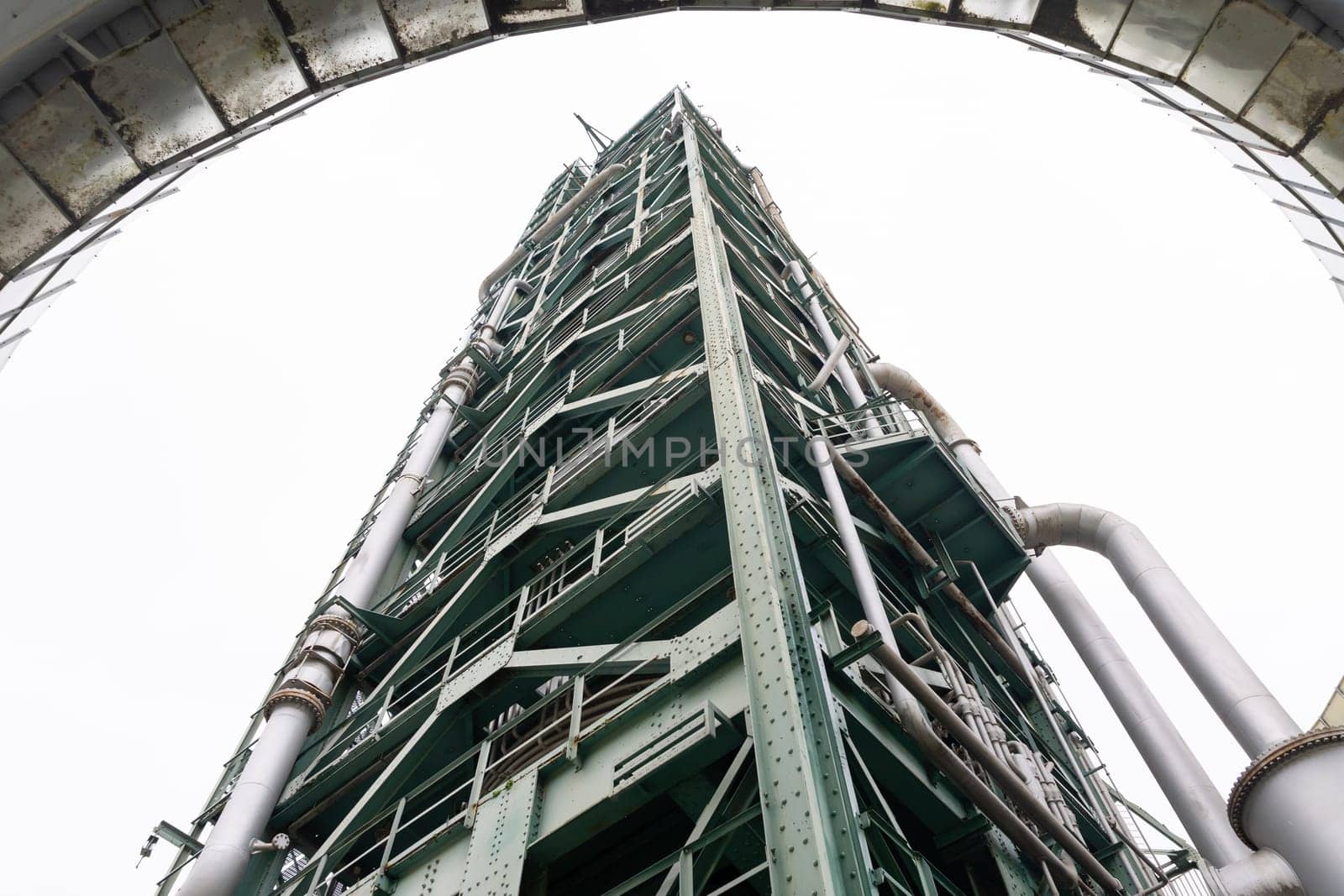 A tall oil refining tower against a gray sky. Mid shot