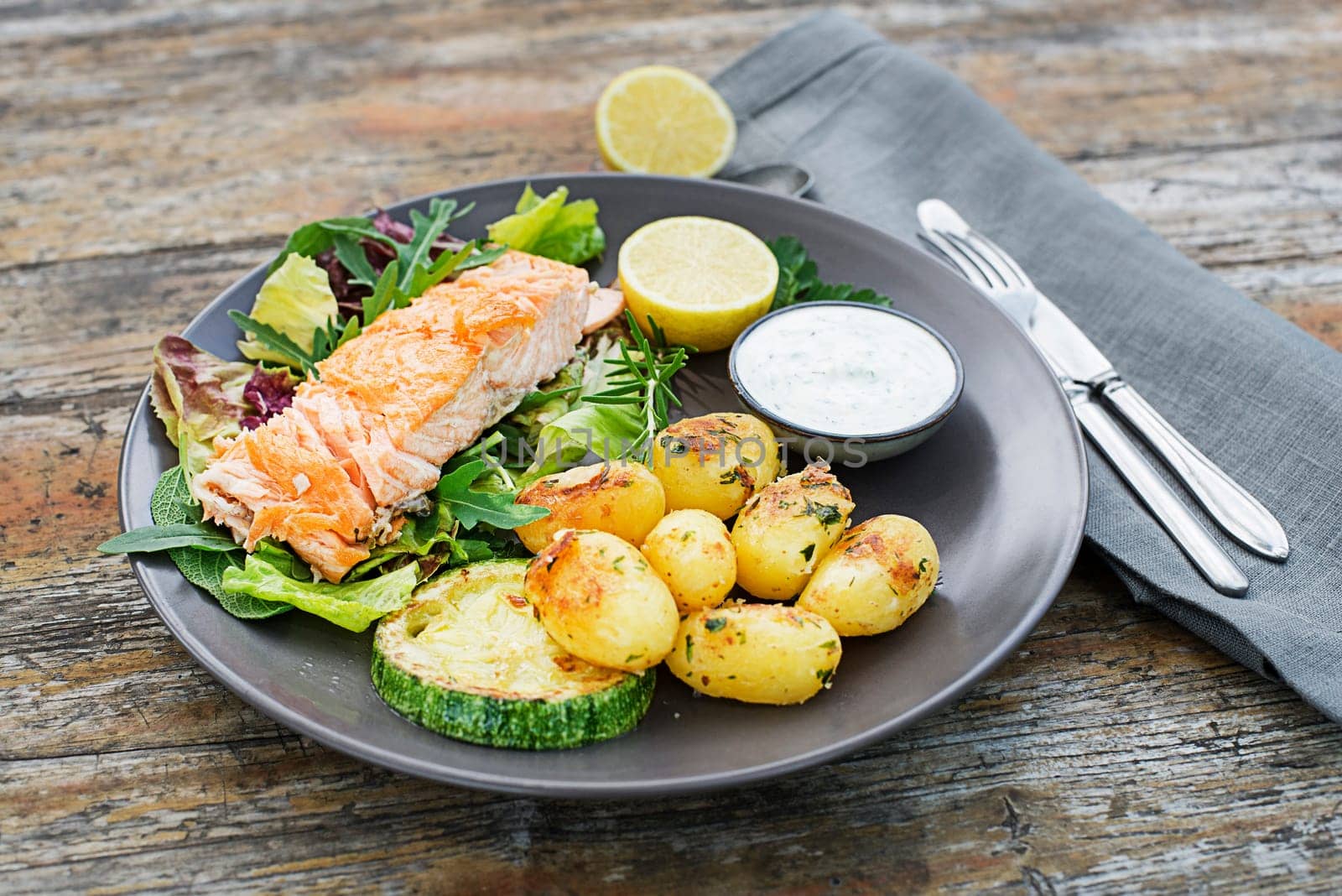 Baked salmon fillet with potatoes and vegetables on wooden table in the garden summer time