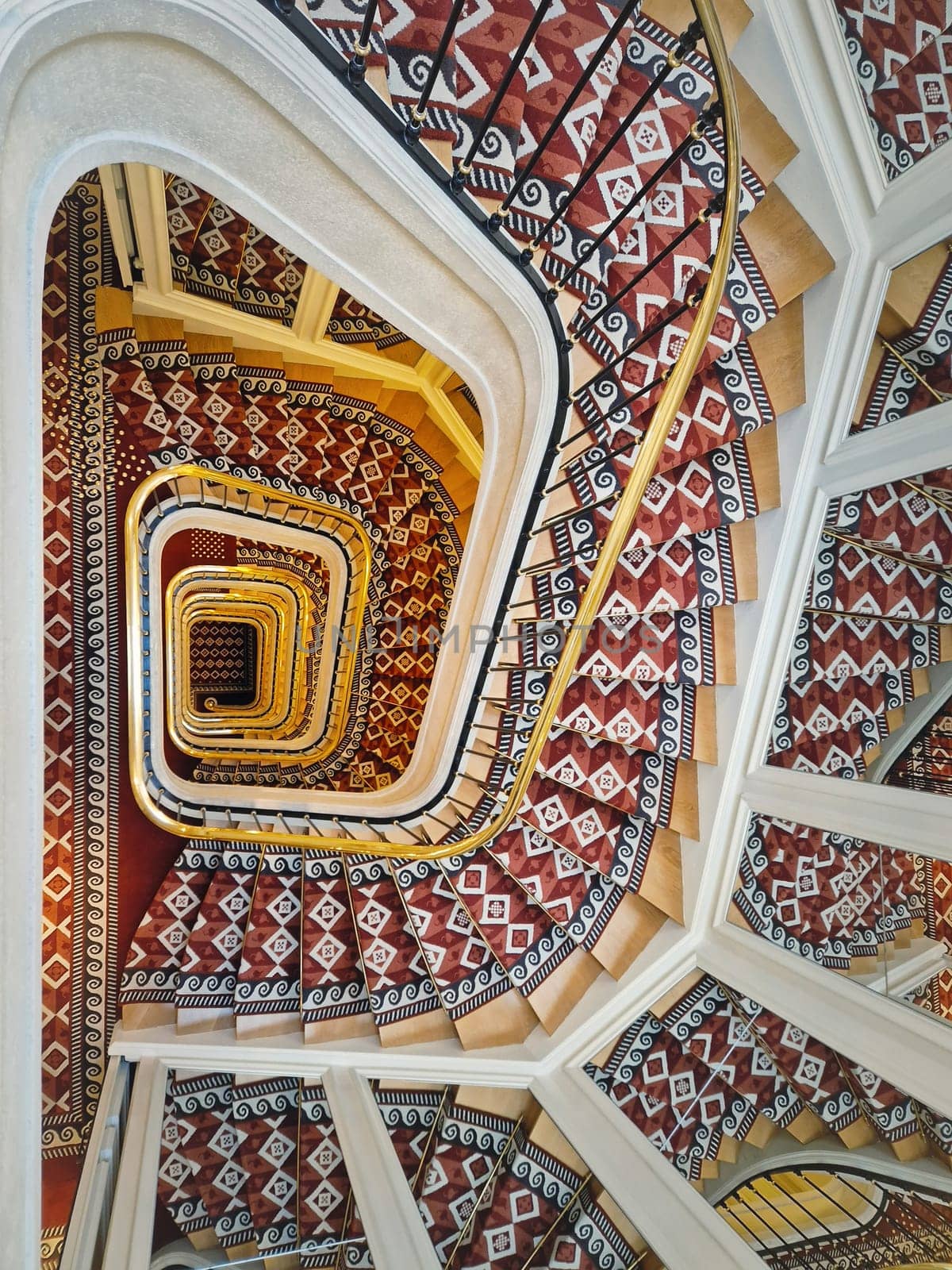 Abstract shape luxurious stairs with red carpet cover and golden handrail. Hypnotic pattern swirl staircase with mirror reflections on the stairwell walls