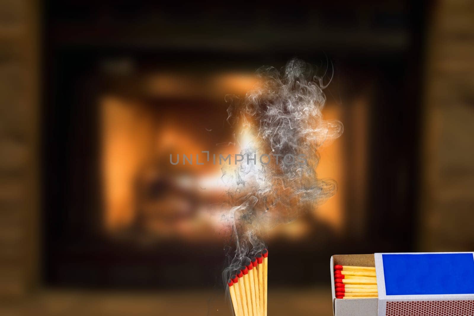 Matches, fire and smoke. A matchbox and rising smoke from several extinguished matches against an abstract blurred fireplace background. Space for copying.