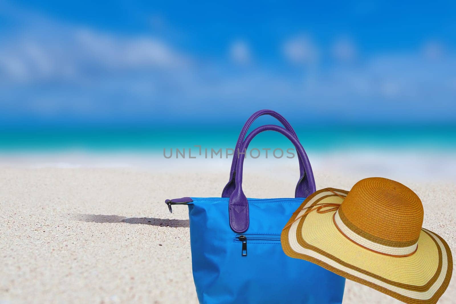 Abstract blurred tropical sunny sandy beach with blue ocean background for travel holiday and beach bag with straw hat for summer holiday.