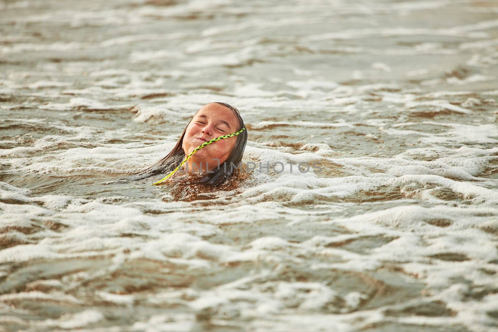 Little girl playing with waves in the sea. Kid playfully splashing in waves. Child jumping in sea. Vacations on the beach. Water splashes. Fun and play during summer vacation. Travel concept